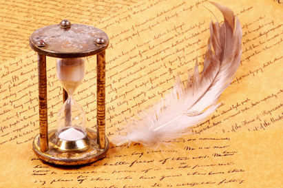 an hourglass and a piece of feather on top of handwritten pages of parchments