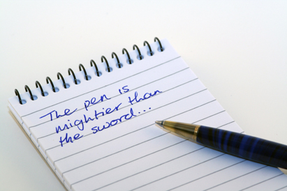 a pen on a notepad with the words 'The pen is mightier than the sword…' written on it