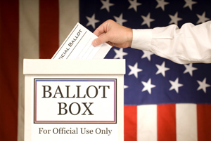 Hand putting a ballot into a ballot box with the United States of America's flag in the background