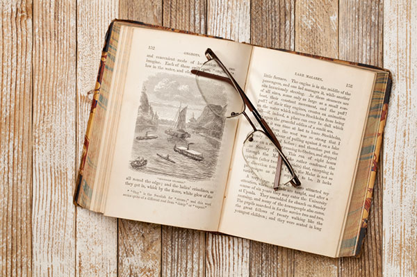 a pair of glasses on an old open book with texts on both pages and an image in the middle of the left page