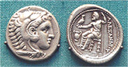 two coins, with one showing the head of a man and the other showing a man sitting on a stool holding a bird